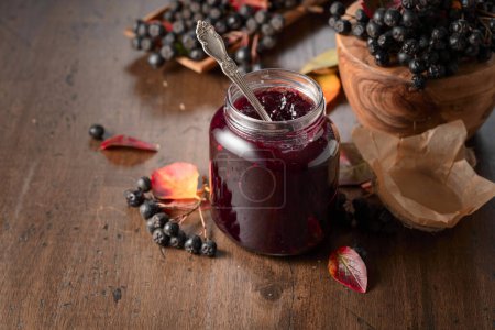Photo for Chokeberry jam and fresh berries with leaves on an old wooden table. - Royalty Free Image