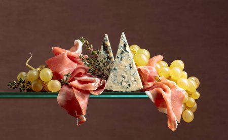 Foto de Uvas con queso azul, jamón y tomillo sobre fondo marrón. - Imagen libre de derechos