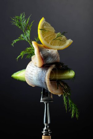 Foto de Filete de arenque en aceite con limón, pepino y eneldo sobre fondo negro. - Imagen libre de derechos