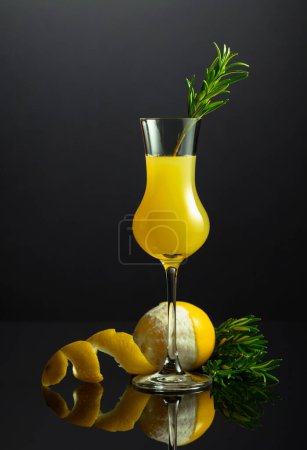 Téléchargez les photos : Liqueur italienne traditionnelle Limoncello avec brindille de romarin sur fond noir réfléchissant. - en image libre de droit
