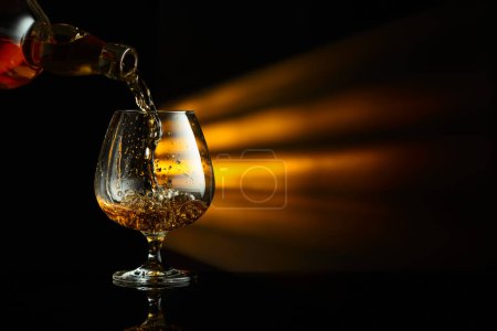 Foto de Verter el brandy de una botella en un snifter sobre un fondo reflectante negro. Copiar espacio. - Imagen libre de derechos