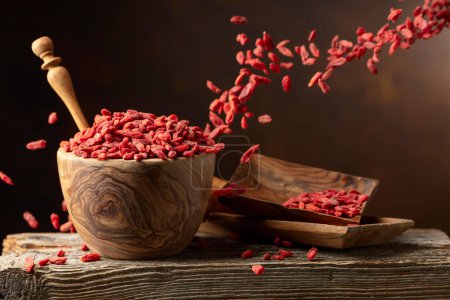 Photo for Dried goji berries in wooden bowl on a brown background. Berries in motion. - Royalty Free Image