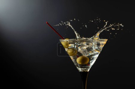 Téléchargez les photos : Verre de cocktail martini sec classique aux olives vertes sur fond noir. Martini aux éclaboussures. Espace libre pour votre texte. - en image libre de droit