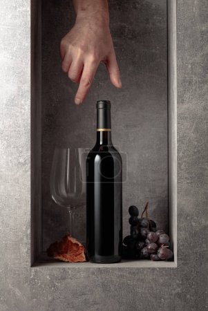 Photo for Bottle of red wine with grapes. Hand reach for a bottle of wine. - Royalty Free Image
