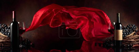 Photo for Bottles of red wine with grapes on a black reflective background. Red satin curtain flutters in the wind. Copy space. - Royalty Free Image