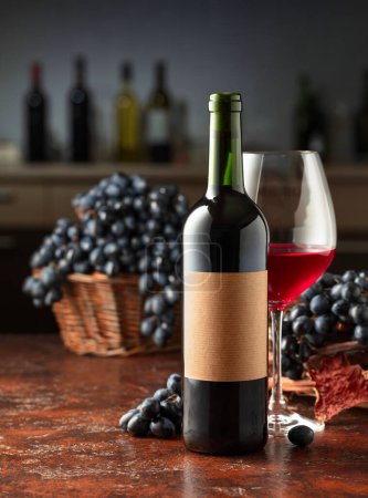 Téléchargez les photos : Bouteille et verre de vin rouge avec des raisins bleus sur une table vintage. Sur une vieille étiquette vide. Dans le comptoir du bar de fond avec diverses bouteilles de vin. - en image libre de droit