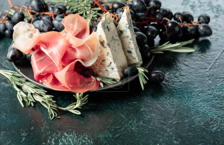 Photo for Prosciutto with blue cheese, grapes, and rosemary, on vintage background. - Royalty Free Image