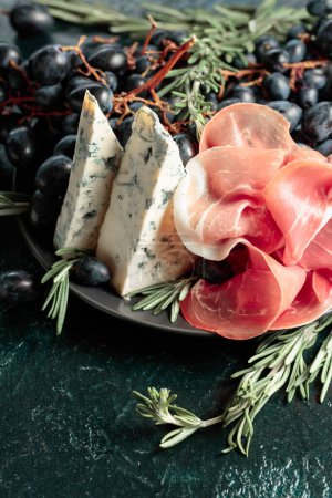Photo for Prosciutto with blue cheese, grapes, and rosemary, on vintage background. - Royalty Free Image
