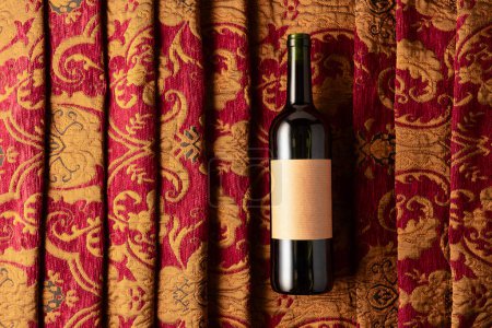 Téléchargez les photos : Bouteille de vin rouge sur une tapisserie rétro à l'ornement floral rouge foncé et doré. Sur une vieille étiquette vide. Vue du dessus. - en image libre de droit