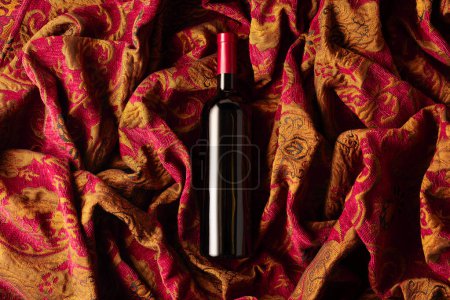 Foto de Botella de vino tinto sobre un tapiz retro con adorno floral rojo oscuro y dorado. Vista superior. - Imagen libre de derechos