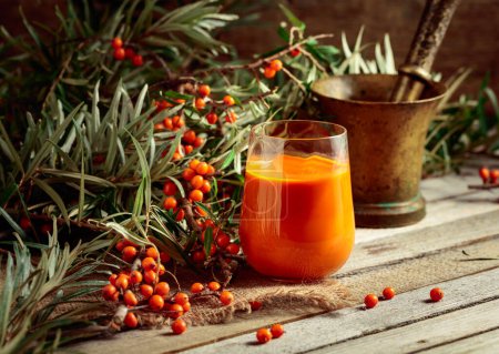 Photo for Glass of sea buckthorn juice and branches with fresh berries on an old wooden table. A healthy vitamin drink. - Royalty Free Image