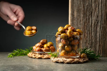 Foto de Aceitunas picantes en un tazón de vidrio. Cuenco con aceitunas conservadas y ramitas de romero sobre una mesa de piedra. - Imagen libre de derechos