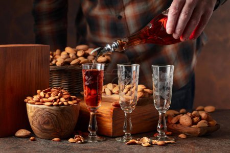 Foto de Licor italiano Amaretto con almendras en una mesa vintage. El licor se vierte de una botella en un vaso. - Imagen libre de derechos