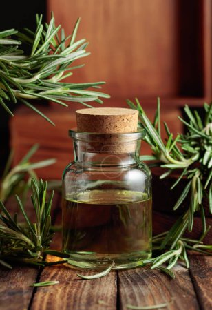 Photo for Rosemary essential oil or infusion on an old wooden table. Aromatherapy, spa, and herbal medicine ingredients. - Royalty Free Image