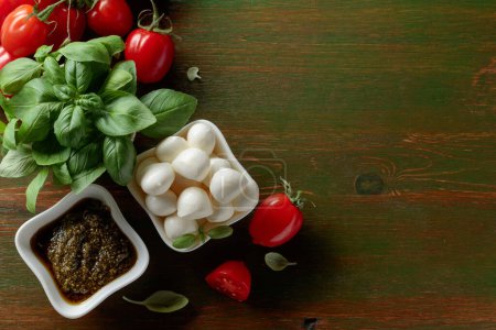 Téléchargez les photos : Fromage mozzarella au basilic, pesto et tomates sur une table en bois vert foncé. Vue du dessus. - en image libre de droit