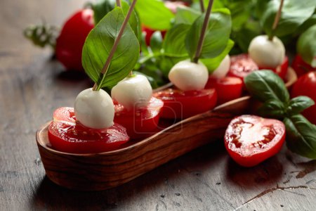 Photo for Mozzarella with basil and tomatoes on an old wooden table. Traditional Italian snack. - Royalty Free Image