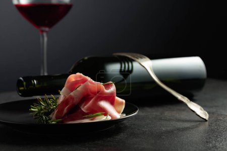 Photo for Prosciutto with rosemary and red wine on a black background. Copy space for your text. - Royalty Free Image