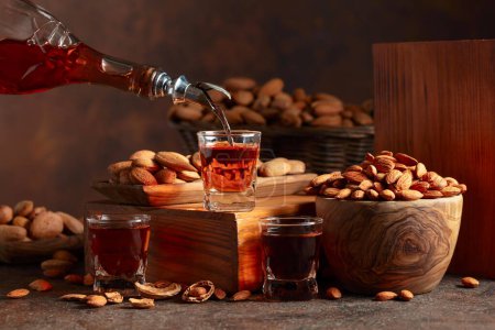 Téléchargez les photos : Liqueur italienne Amaretto aux amandes noix sur une table vintage. La liqueur est versée d'une bouteille dans un verre. - en image libre de droit