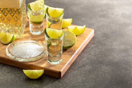 Foto de Tequila de oro con sal marina y rodajas de lima en una tabla de cortar. - Imagen libre de derechos