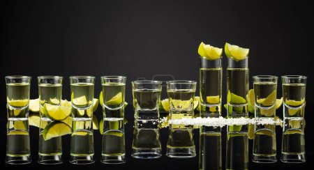 Téléchargez les photos : Tequila photos avec des tranches de citron vert et du sel sur un fond réfléchissant noir. Espace de copie. - en image libre de droit
