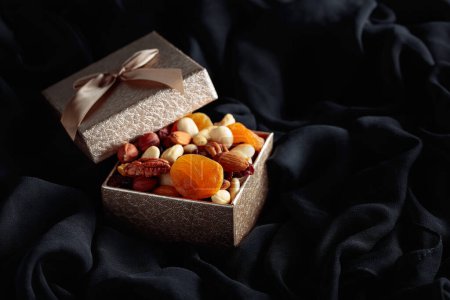 Foto de Frutas secas y frutos secos en una caja de regalo sobre un paño negro. - Imagen libre de derechos