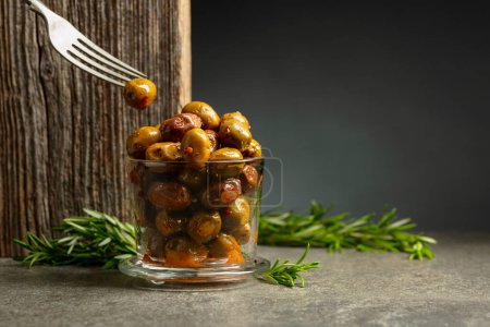 Photo for Spicy olives in a glass bowl. Bowl with preserved olives and rosemary twigs on a stone table. - Royalty Free Image