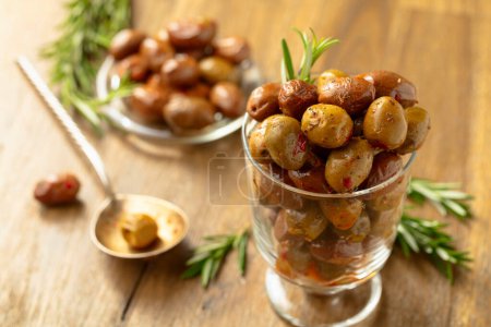 Téléchargez les photos : Olives épicées dans un bol en verre. Bol avec olives conservées et brindilles de romarin sur une table en bois. - en image libre de droit
