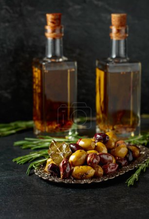 Foto de Spicy olives and bottles of olive oil. on a black stone table. - Imagen libre de derechos