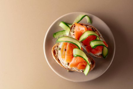 Photo for Sandwiches with smoked trout, cream cheese, fresh cucumber and capers on a beige background. Top view, copy space. - Royalty Free Image