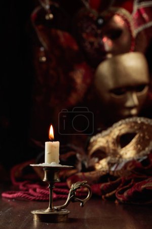 Foto de Vela ardiente en un viejo candelabro de latón y máscaras de carnaval en una vieja mesa de madera. - Imagen libre de derechos
