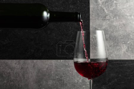 Foto de El vino tinto se vierte de la botella en una copa. Fondo de piedra gris y negro. Copiar espacio. - Imagen libre de derechos