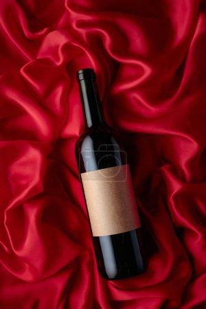 Foto de Bottle of red wine with an empty label on a satin background. Top view. - Imagen libre de derechos
