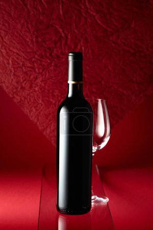 Photo for Bottle of red wine and an empty wine glass on a red background. - Royalty Free Image