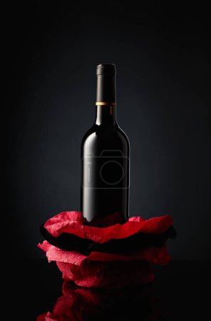 Foto de Bottle of red wine on a crumpled paper. Black reflective background. - Imagen libre de derechos