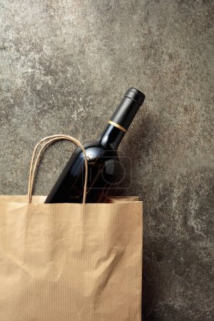 Téléchargez les photos : Sac à provisions en papier avec une bouteille de vin rouge sur un vieux fond de pierre. Vue du dessus, espace de copie. - en image libre de droit
