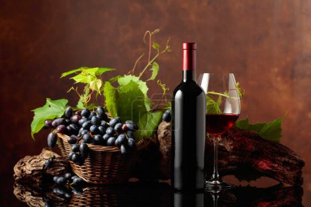 Foto de Copa y botella de vino tinto con uvas azules y ramas de vid. Copiar espacio. - Imagen libre de derechos