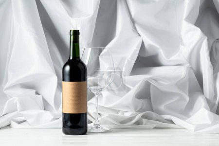 Photo for Red wine on a white wooden tfble. In the background white satin curtain. - Royalty Free Image
