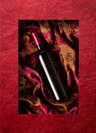 Photo for Bottle of red wine on a retro tapestry with dark red and golden floral ornament. Top view. - Royalty Free Image