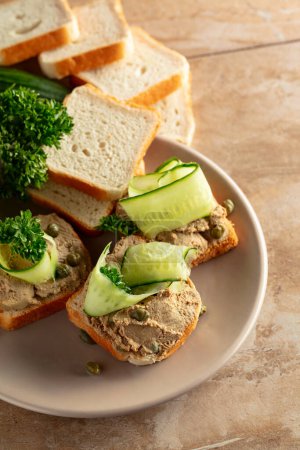 Photo for Toasts with pate on a beige plate. Open sandwiches with pate, fresh cucumber, capers, and parsley. - Royalty Free Image