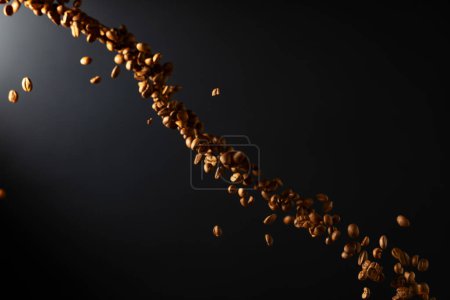 Téléchargez les photos : Grains de café en mouvement sur un fond noir. Fond déconcentré pour votre produit. Espace de copie. - en image libre de droit