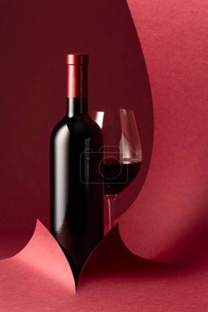 Photo for Bottle and glass of red wine on a red background. Copy space. - Royalty Free Image
