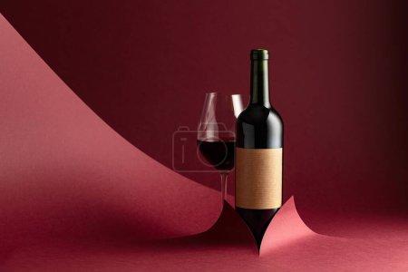 Téléchargez les photos : Bouteille et verre de vin rouge sur fond rouge. Sur une étiquette vide. Espace de copie. - en image libre de droit