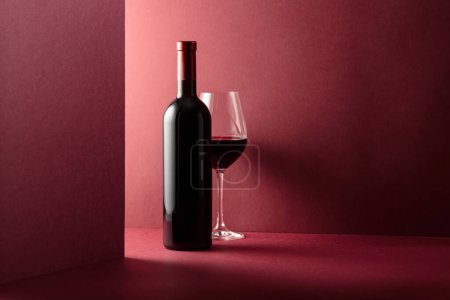 Téléchargez les photos : Bouteille et verre de vin rouge sur fond rouge. Espace de copie
. - en image libre de droit