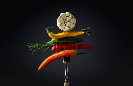 Foto de Red hot chili peppers with garlic and rosemary on a fork. Concept of spicy food. - Imagen libre de derechos