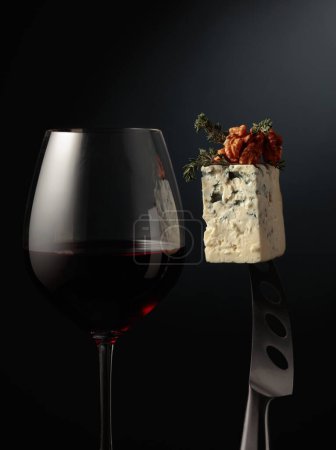 Foto de Un vaso de vino tinto y queso azul. Queso con nueces y tomillo en un cuchillo. - Imagen libre de derechos