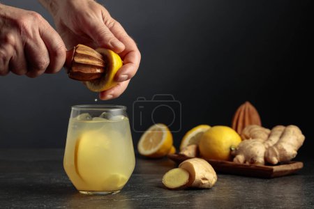 Photo for Ginger Ale with ice and lemon. Juice is squeezed out of a lemon with an old wooden juicer. - Royalty Free Image