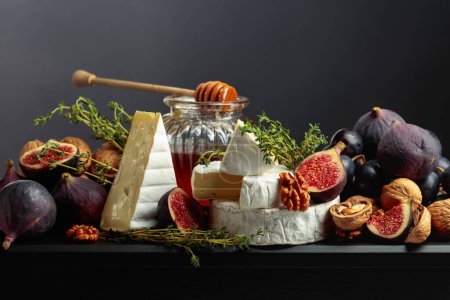 Photo for Camembert cheese with figs, grapes, walnuts, honey, and thyme. Soft cheese with fruits on a black background. - Royalty Free Image