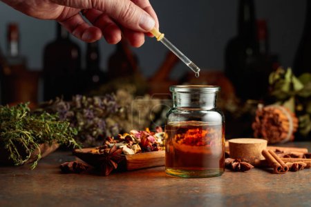 Photo for Dropping essential herbal tincture into a small glass bottle. On a table dried herbs, flowers, spices, and old kitchen utensils. Concept of herbal medicine. - Royalty Free Image