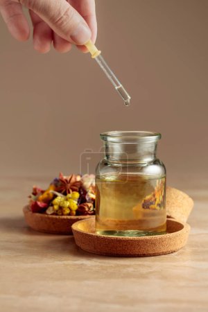 Photo for Dropping essential oil or herbal tincture into a glass bottle. Mix of dried healthy medicinal herbs and healing plants on a beige background. Copy space. - Royalty Free Image