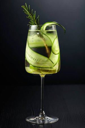 Photo for Gin tonic with ice, rosemary, lime, and cucumber in frosted glass. Glass with a cocktail on a black background. - Royalty Free Image